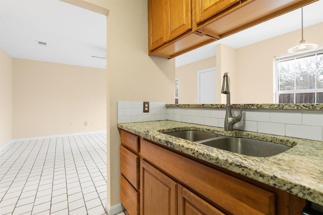 kitchen with decorative light fixtures, sink, backsplash, light tile patterned floors, and light stone countertops