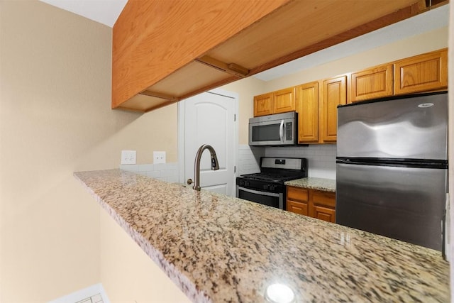 kitchen featuring sink, light stone counters, appliances with stainless steel finishes, kitchen peninsula, and decorative backsplash