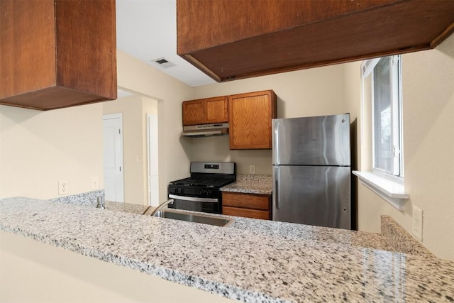 kitchen with light stone counters, appliances with stainless steel finishes, kitchen peninsula, and sink