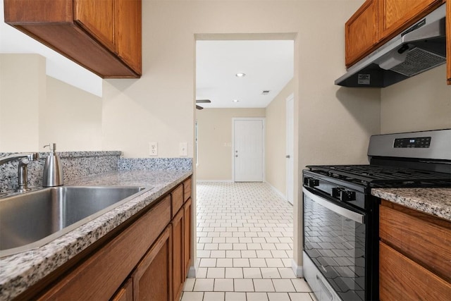 kitchen with light tile patterned flooring, stainless steel range with gas stovetop, light stone countertops, and sink