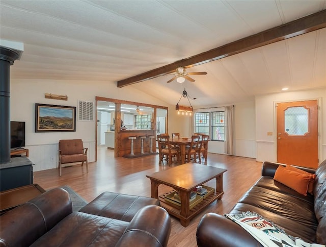 living room with ceiling fan, light hardwood / wood-style floors, lofted ceiling with beams, and a wood stove