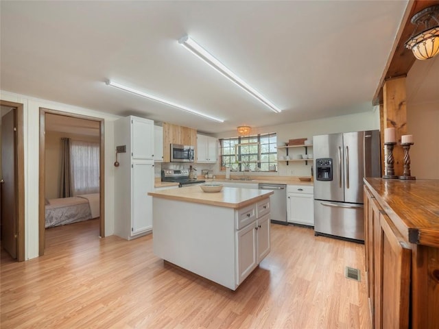 kitchen with a kitchen island, light wood-type flooring, white cabinets, and appliances with stainless steel finishes