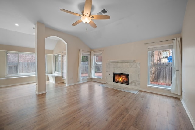 unfurnished living room with ceiling fan, lofted ceiling, a tile fireplace, and light wood-type flooring