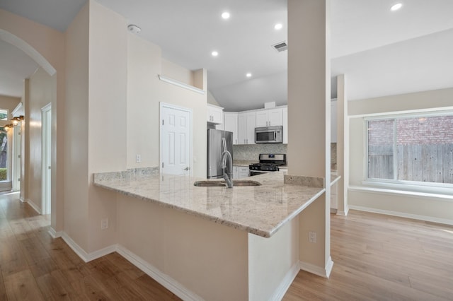 kitchen with sink, stainless steel appliances, light stone countertops, white cabinets, and kitchen peninsula