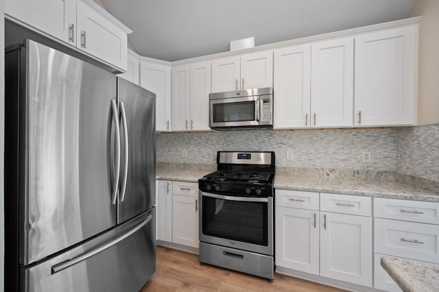 kitchen with appliances with stainless steel finishes, white cabinetry, light stone counters, tasteful backsplash, and light wood-type flooring