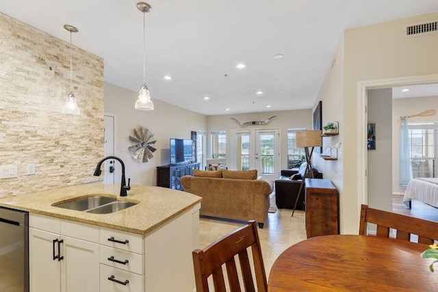 kitchen featuring dishwasher, sink, hanging light fixtures, light stone countertops, and french doors