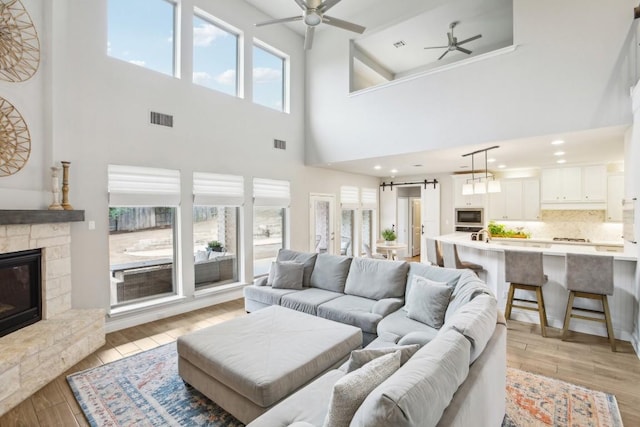 living room with a stone fireplace, a barn door, ceiling fan, and light wood-type flooring