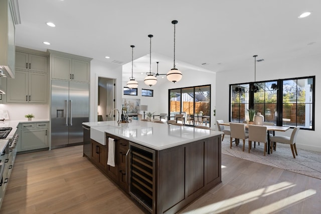 kitchen featuring wine cooler, sink, built in refrigerator, an island with sink, and pendant lighting