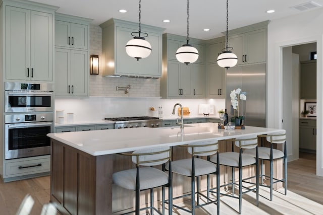 kitchen with sink, tasteful backsplash, hanging light fixtures, a center island with sink, and appliances with stainless steel finishes