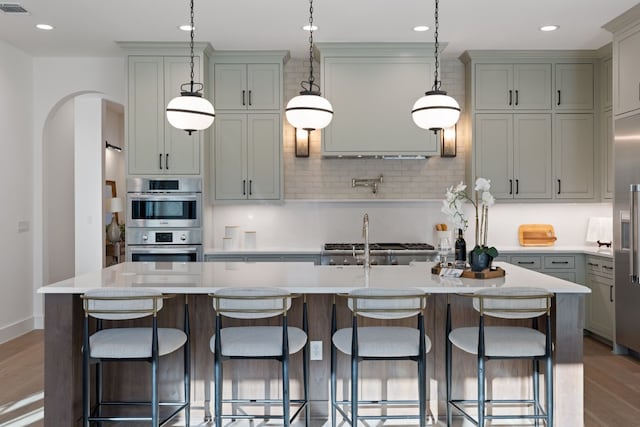 kitchen with a breakfast bar area, gray cabinetry, decorative light fixtures, stainless steel appliances, and a kitchen island with sink