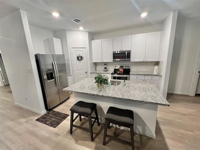 kitchen with a kitchen bar, white cabinetry, appliances with stainless steel finishes, an island with sink, and light stone countertops