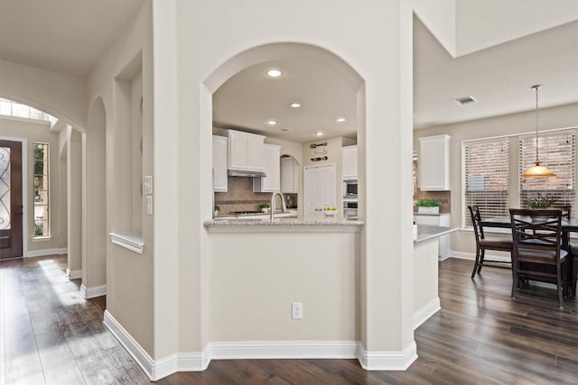 kitchen with light stone counters, decorative light fixtures, dark hardwood / wood-style flooring, and white cabinets