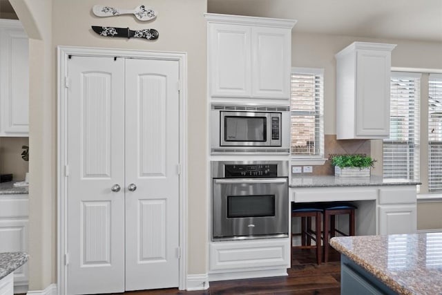 kitchen featuring white cabinetry, stainless steel appliances, dark hardwood / wood-style floors, tasteful backsplash, and light stone countertops