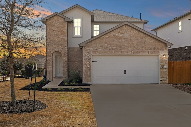 traditional-style house featuring brick siding, concrete driveway, an attached garage, fence, and stucco siding