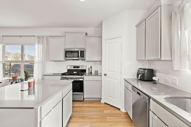 kitchen with tasteful backsplash, stainless steel appliances, sink, and light hardwood / wood-style flooring