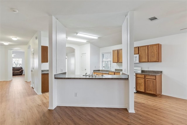 kitchen with kitchen peninsula, sink, light hardwood / wood-style flooring, and stove