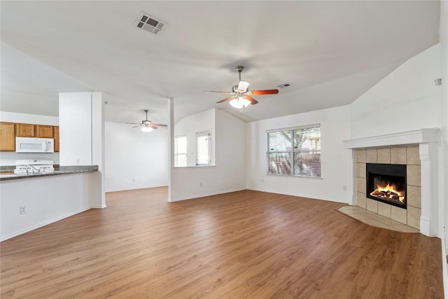 unfurnished living room featuring ceiling fan, light hardwood / wood-style floors, vaulted ceiling, and a tile fireplace