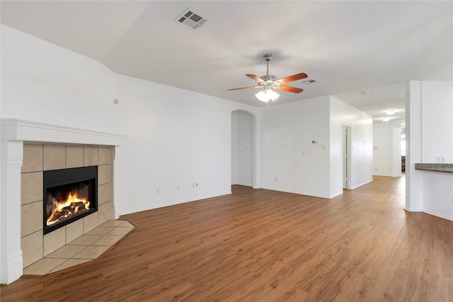 unfurnished living room featuring a tiled fireplace, ceiling fan, and light wood-type flooring