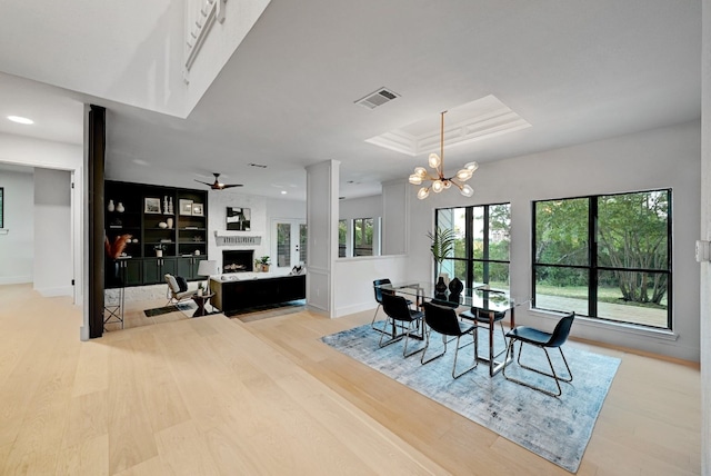 dining room featuring light hardwood / wood-style flooring, ceiling fan with notable chandelier, and a fireplace