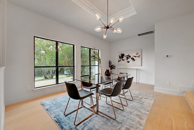 dining room featuring a raised ceiling, a notable chandelier, and light wood-type flooring