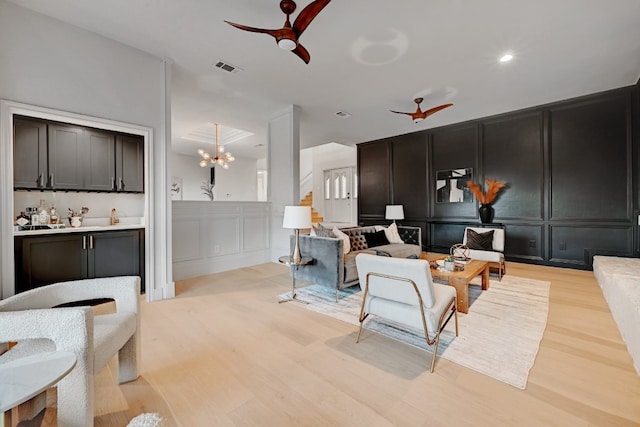 living room with light hardwood / wood-style floors and ceiling fan with notable chandelier