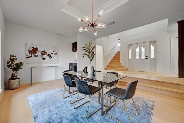 dining area featuring crown molding, a notable chandelier, a tray ceiling, and light wood-type flooring