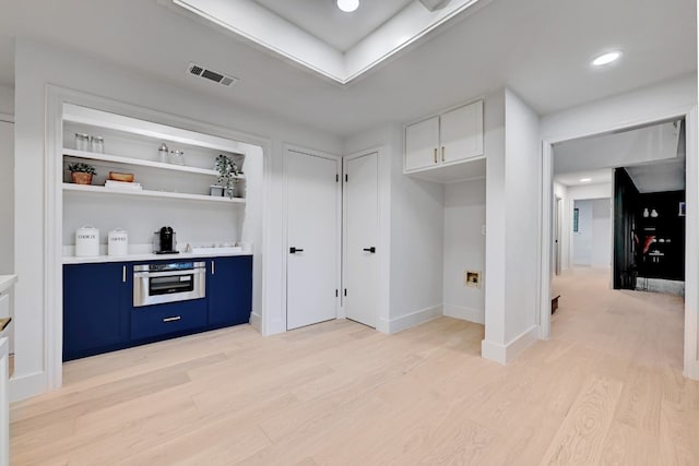 interior space featuring blue cabinetry, stainless steel oven, white cabinets, and light wood-type flooring