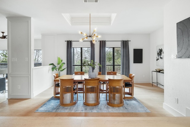 dining space with crown molding, a raised ceiling, visible vents, light wood-style floors, and a chandelier