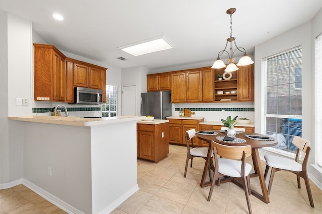 kitchen featuring stainless steel appliances, kitchen peninsula, backsplash, and decorative light fixtures