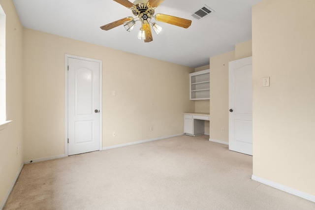 unfurnished room with light carpet, built in desk, and ceiling fan