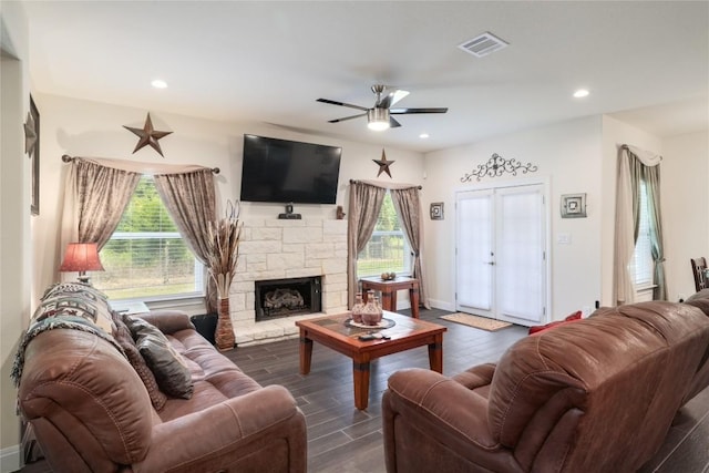 living room featuring a healthy amount of sunlight, dark wood-style floors, visible vents, and a stone fireplace