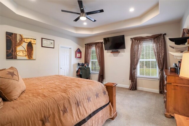 bedroom with ceiling fan, a tray ceiling, and light carpet