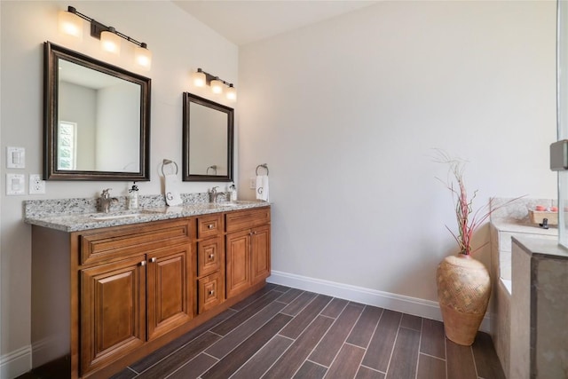 full bathroom with double vanity, wood finish floors, a sink, and baseboards