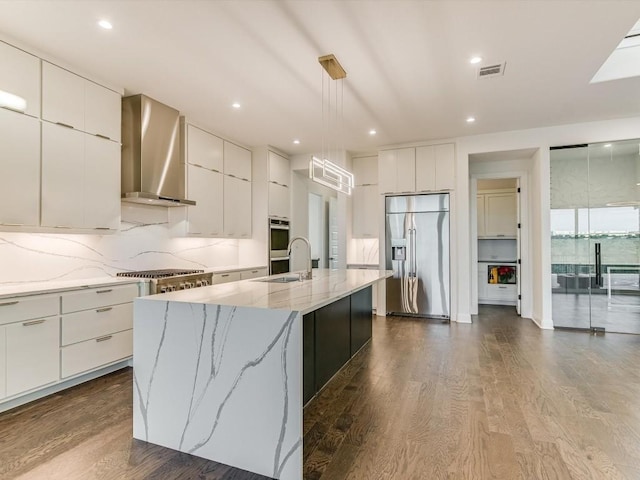 kitchen featuring a spacious island, appliances with stainless steel finishes, pendant lighting, wall chimney range hood, and white cabinets