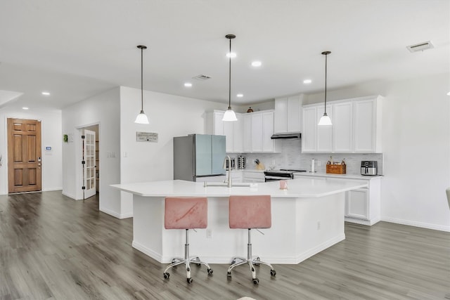 kitchen with appliances with stainless steel finishes, white cabinets, a kitchen bar, decorative backsplash, and a large island with sink