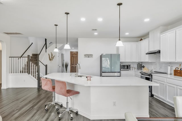 kitchen featuring sink, appliances with stainless steel finishes, white cabinetry, hardwood / wood-style floors, and an island with sink