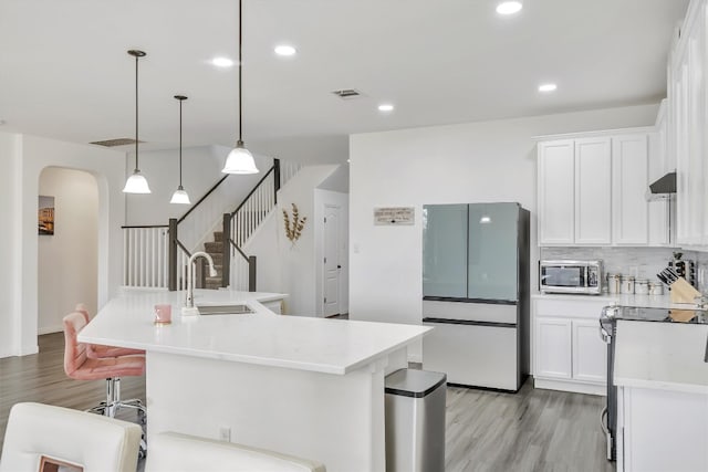 kitchen featuring sink, fridge, white cabinets, a center island with sink, and decorative light fixtures