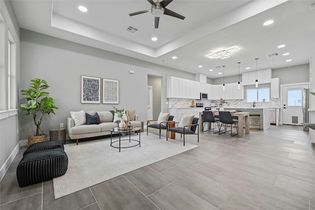 living room with ceiling fan, a tray ceiling, and sink