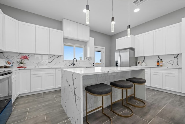 kitchen featuring sink, hanging light fixtures, appliances with stainless steel finishes, a kitchen island, and white cabinets