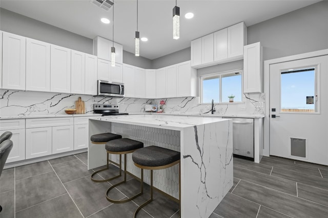 kitchen featuring pendant lighting, a kitchen island, white cabinets, and appliances with stainless steel finishes