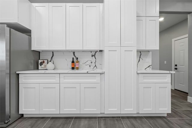 kitchen featuring light stone counters, stainless steel refrigerator, and white cabinets