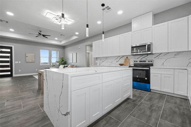 kitchen featuring stainless steel appliances, a tray ceiling, a center island, and white cabinets