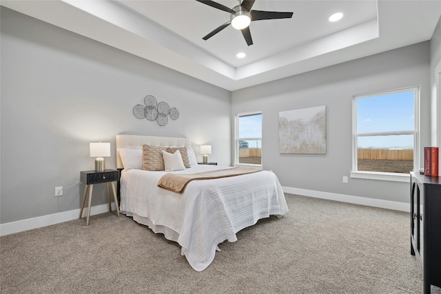 carpeted bedroom with a raised ceiling and ceiling fan