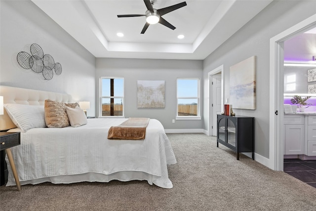 bedroom with ceiling fan, dark carpet, and a tray ceiling