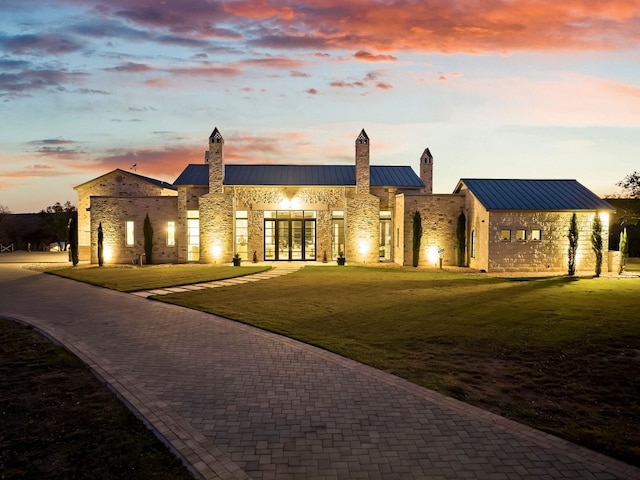 view of front of property with a standing seam roof, a front lawn, french doors, stone siding, and metal roof