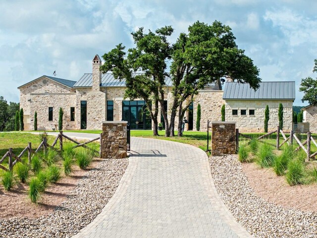 view of front of property featuring fence, a standing seam roof, stone siding, decorative driveway, and metal roof