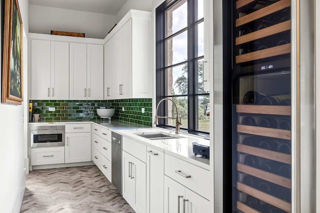 kitchen with beverage cooler, a sink, tasteful backsplash, stainless steel dishwasher, and white cabinetry