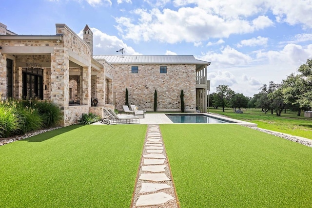 rear view of property featuring a lawn, metal roof, a balcony, an outdoor pool, and a patio