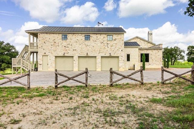 back of property with driveway, a standing seam roof, stone siding, stairway, and metal roof