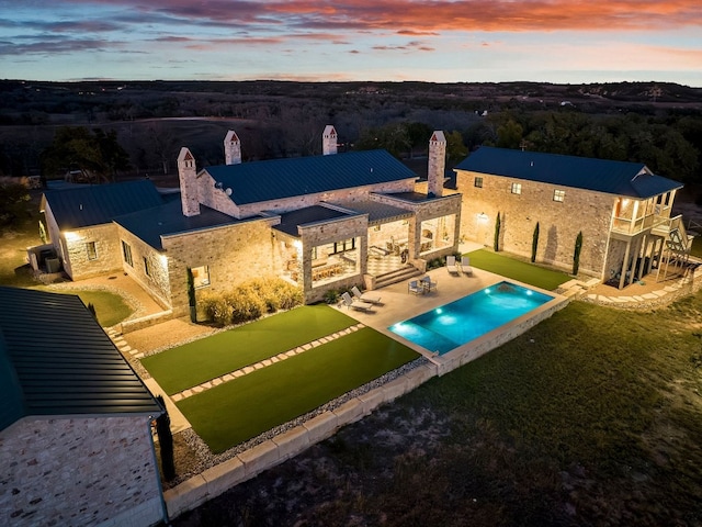 pool at dusk with an outdoor pool, a patio area, a lawn, and a fenced backyard